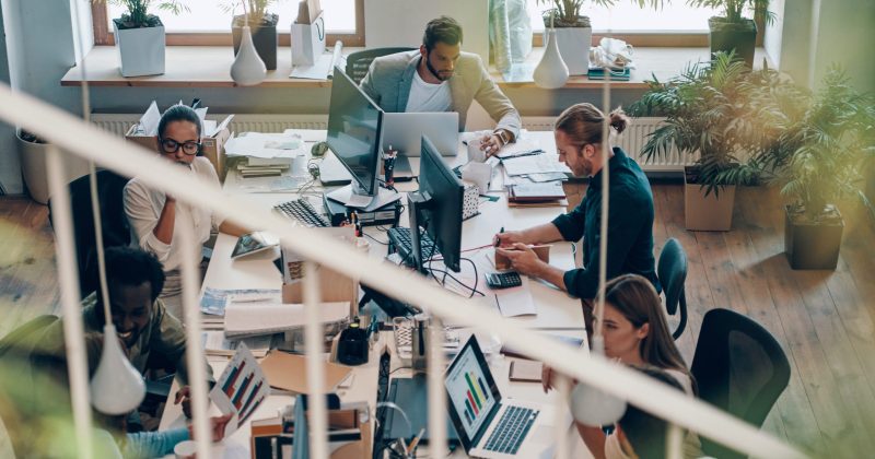 Top view of young modern people in smart casual wear communicating and using modern technologies while working in the office