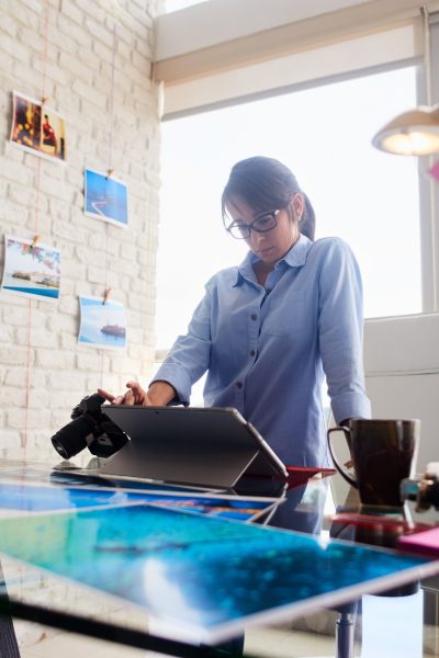 Young people, small business, technology. Woman at work as photographer in office. Hispanic girl using computer laptop for image review, editing.